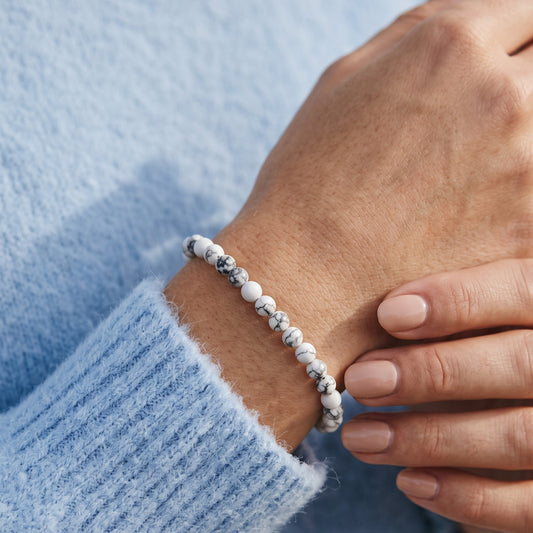 A close-up of a person's wrist wearing a beaded bracelet made of white and gray marbled beads, paired with a light blue knit sweater.