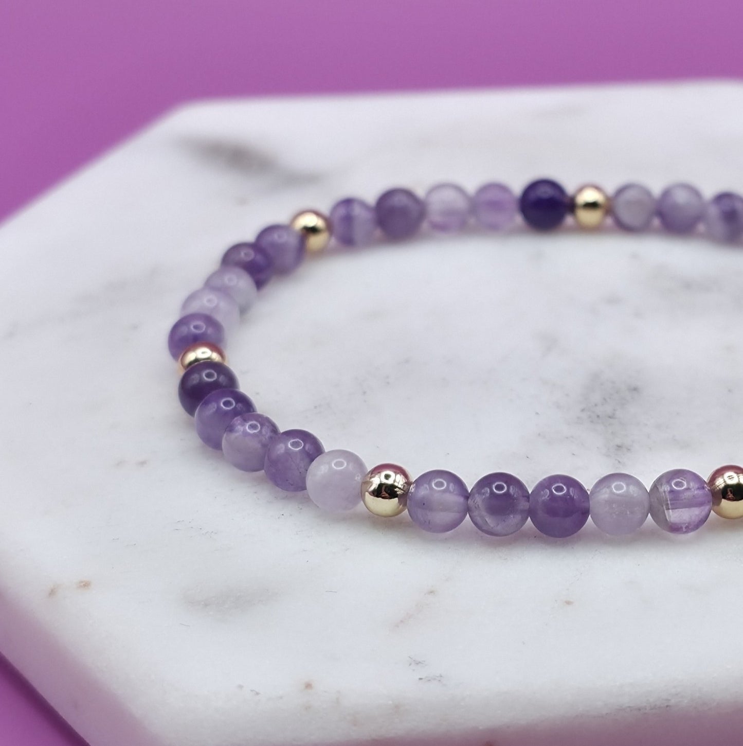 Handmade natural Amethyst beaded bracelet with gold accent beads, 4mm beads laying flat on a marble plate.