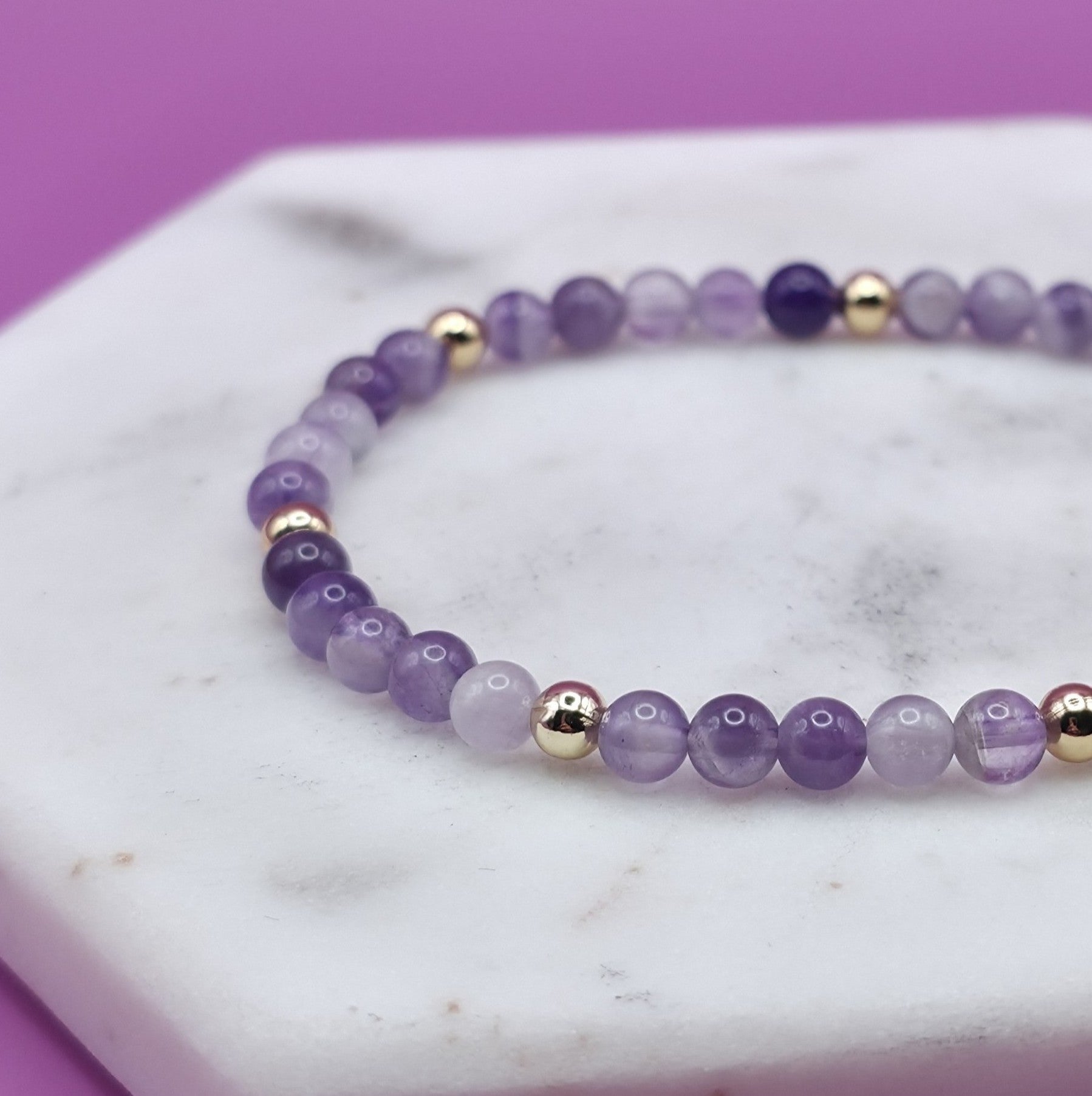 Handmade natural Amethyst beaded bracelet with gold accent beads, 4mm beads laying flat on a marble plate.
