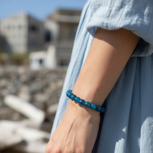 Model wearing handmade natural Blue Apatite beaded bracelet, 8mm beads with a pale blue dress and a coastal scene in the background.