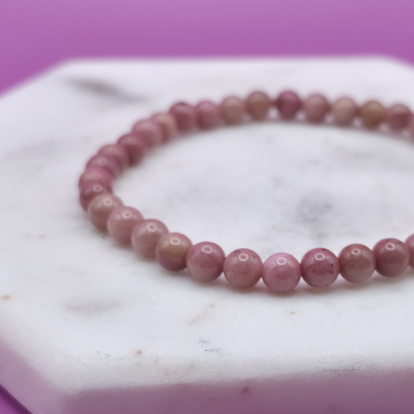Handmade natural Rhodonite beaded bracelet, 4mm beads laying flat on a marble plate