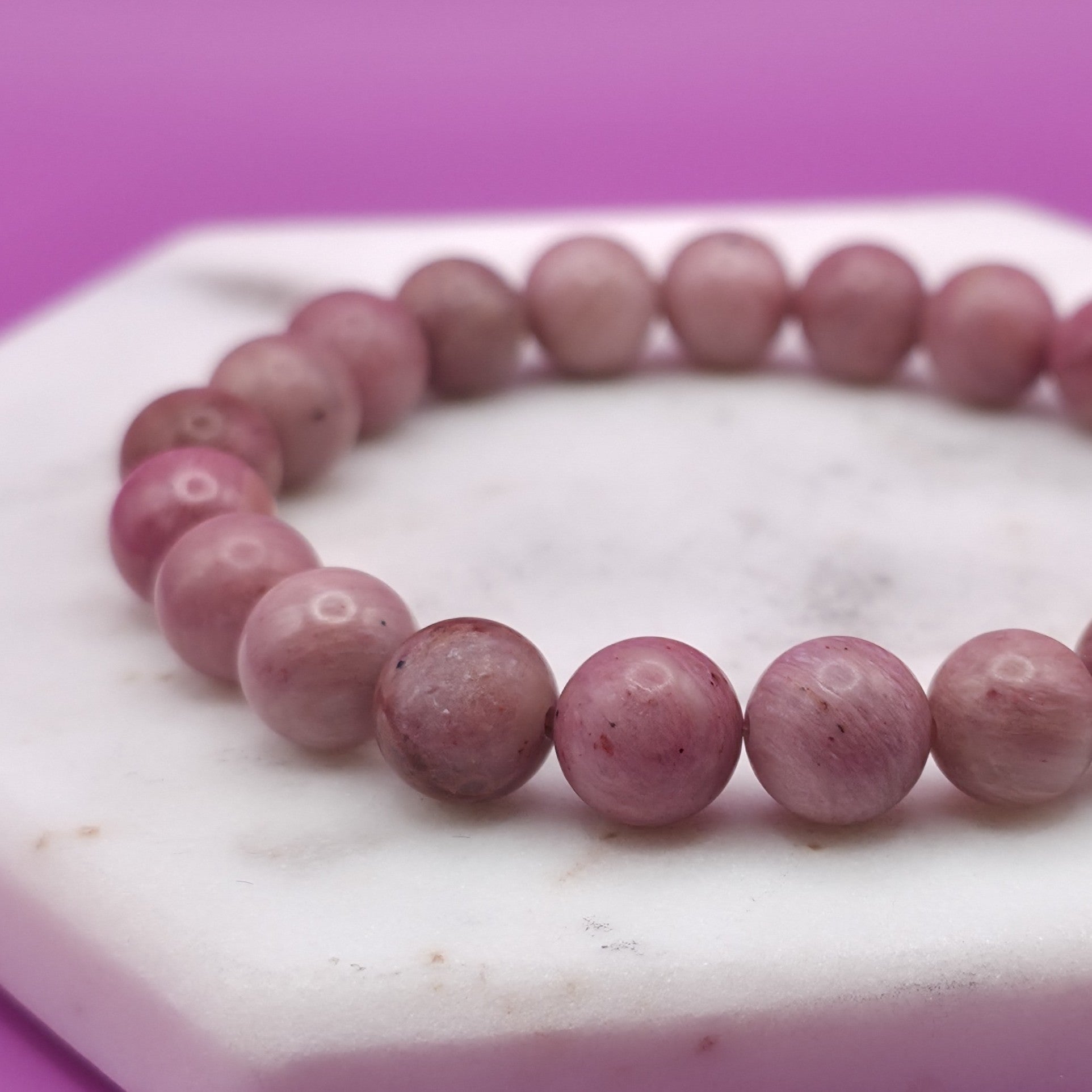 Handmade natural Rhodonite beaded bracelet, 8mm beads laying flat on a marble plate.